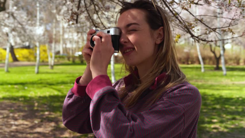 Young woman taking photos with a vintage camera of a blossoming tree in springtime
