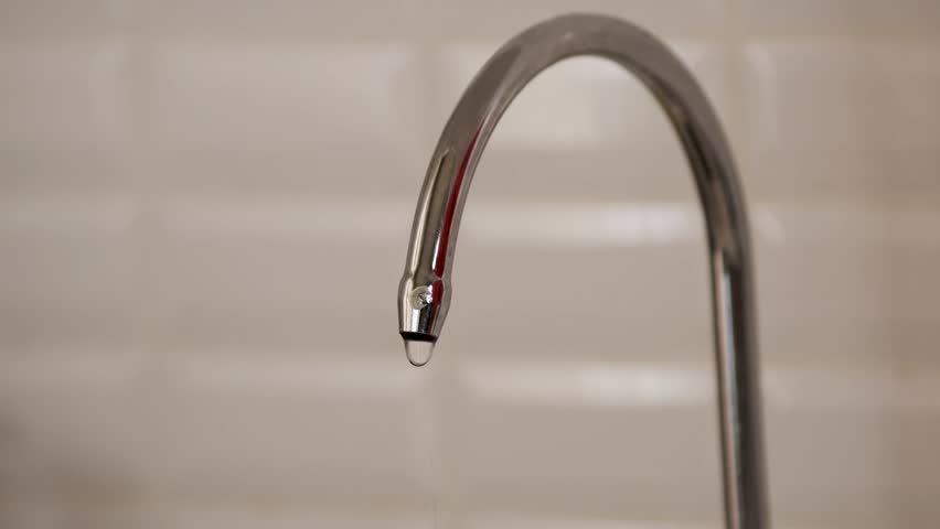 Slow dripping water drops from a leaking chrome faucet in a bathroom or kitchen