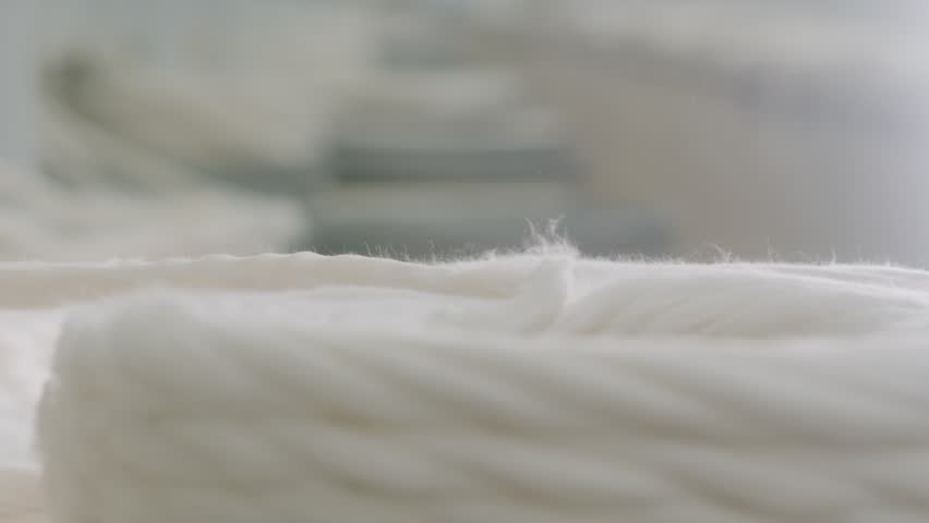 Close-up of cotton sliver production in a textile spinning mill. Detailed view of raw white cotton fibers being processed and coiled during the carding stage of garment manufacturing