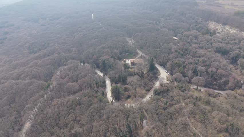 Drone shot of curved dirt road crossing forest terrain with dry vegetation and hills landscape