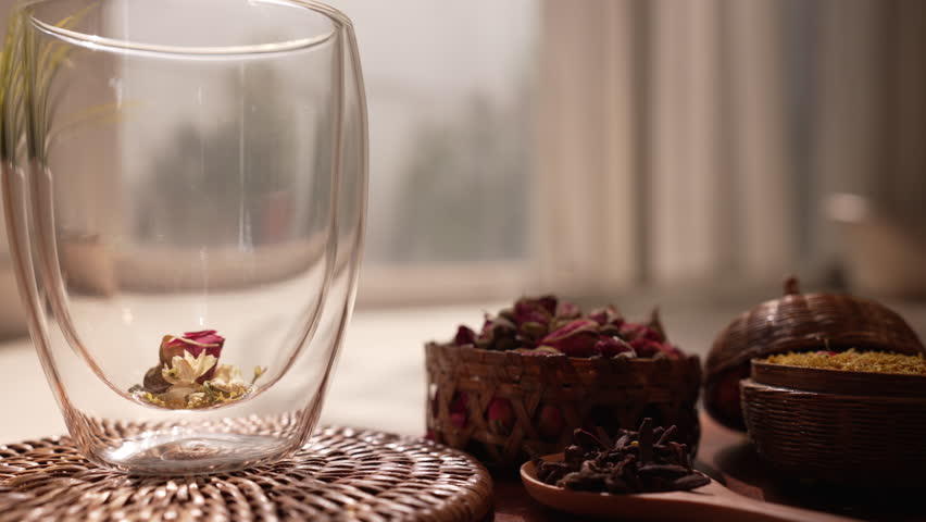 Cinematic close-up of pouring hot water over flower tea in a glass, revealing steam and rising botanical ingredients on a rustic table in a sunlit room for a wellness brewing ritual.