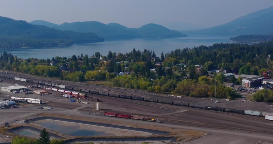 Residential neighborhood near Whitefish Lake with forest and mountains surrounding railroad tracks, Whitefish Montana, aerial drone