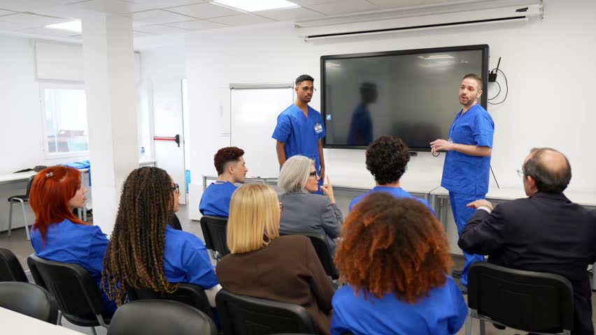 Two male surgeons presenting a lecture on a fractured bone x ray to a diverse group of medical students and professionals during a training session in a modern hospital conference room