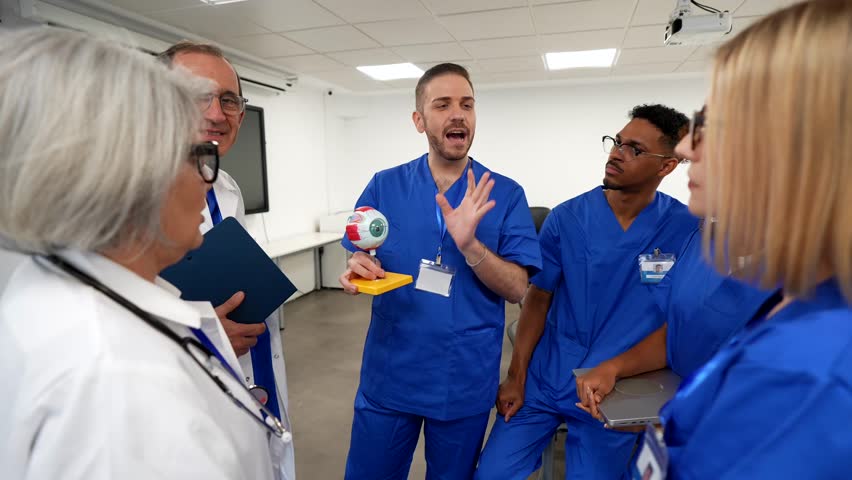 Young ophthalmology professor teaching a lesson on the human eye anatomy to a group of medical interns, using an anatomical model during a training course in a modern hospital classroom
