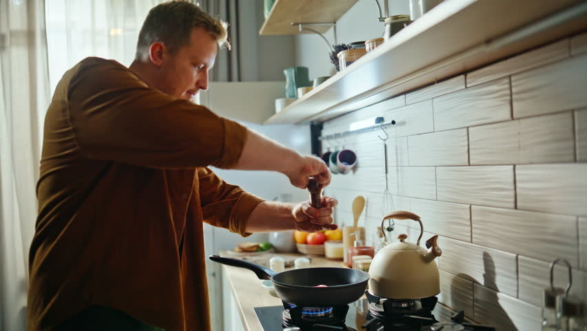 Man salting tasty dish in frying pan cooking healthy nutritious food domestic kitchen closeup. Young chef using wooden spatula turning over grilling meat steak. Guy preparing delicious home meal.