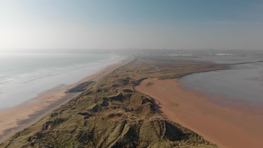Aerial view of coastal town at Tramore, Ireland, with sand dunes, marshland, and serene natural landscape, bathed in soft light.