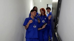 Diverse group of smiling male and female medical students in blue scrubs walking down the stairs in a hospital corridor, laughing and chatting together during a break from their studies - Powered by Shutterstock - Get 15% off with code: PIKWIZARD15