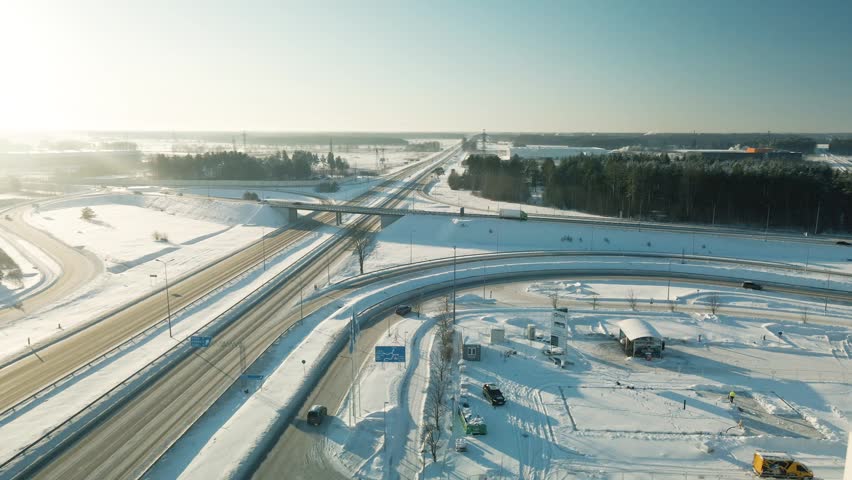 Bright sunshine illuminating a modern highway interchange with cars and trucks driving through a beautiful snowy winter landscape, revealing the complex road network from an aerial perspective