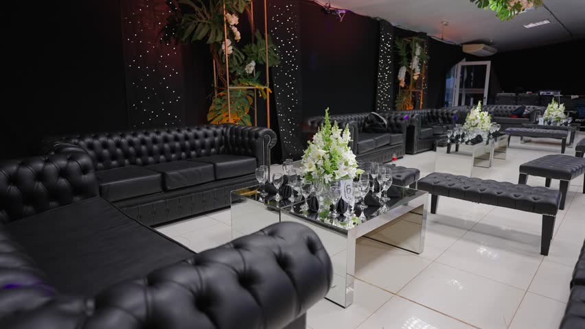 Slow motion right side orbit of a luxury wedding lounge featuring black Chesterfield sofas and a floral centerpiece against a star wall.