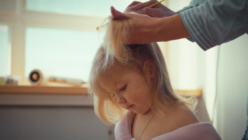 With tender care, a young mother gently works a comb through her little one's tangled locks, patiently straightening strands as she skillfully gathers hair into neat ponytails
