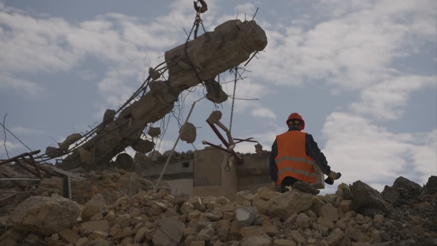 Dismantling of the old building. The worker is watching. Crane lifting concrete beam