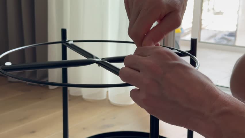 Hands tighten bolt using hex key on metal frame during table assembly. Fingers screw fastener into structure while building furniture at home. Concept diy, setup, interior.