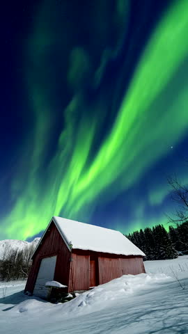 Aurora borealis swirls above a snowy barn near Tromso, Norway, winter night, static tripod timelapse.