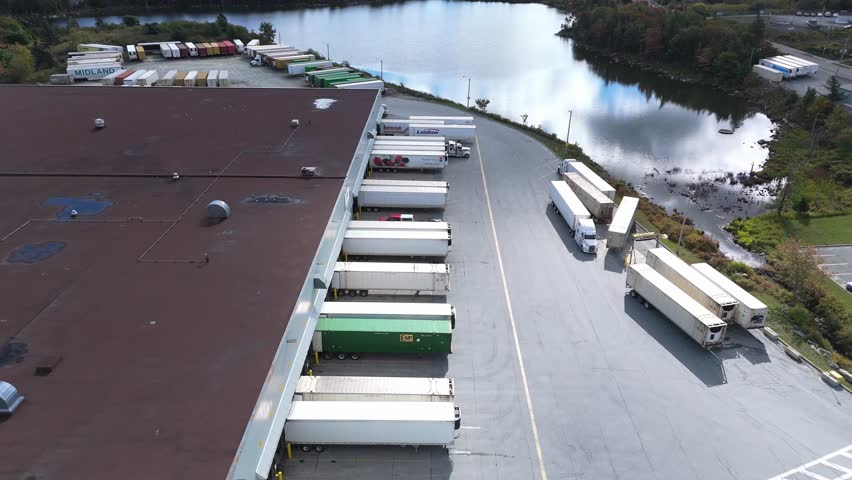 High-angle aerial view of a large logistics and distribution center in Halifax, Nova Scotia. Multiple semi-trucks with trailers docked at loading bays, extensive warehouse facility, Canadian freight 