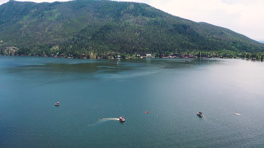 Drone shot over Grand Lake Colorado showing sailboats, motorboats, wooded peninsulas, and shoreline neighborhoods spread across the scenic alpine water in summer light