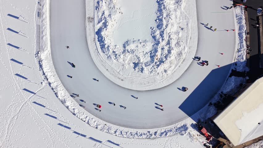 Cinematic drone aerial view on a sunny November day: crowds of people joyfully ice skating on the outdoor oval rink in downtown Halifax, Nova Scotia, Canada. Vibrant winter scene with golden sunlight 