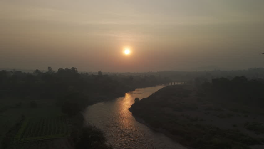 Morning sun rises over a misty meandering river, reflecting vibrant colours in the water. hazy monsoon sunrise