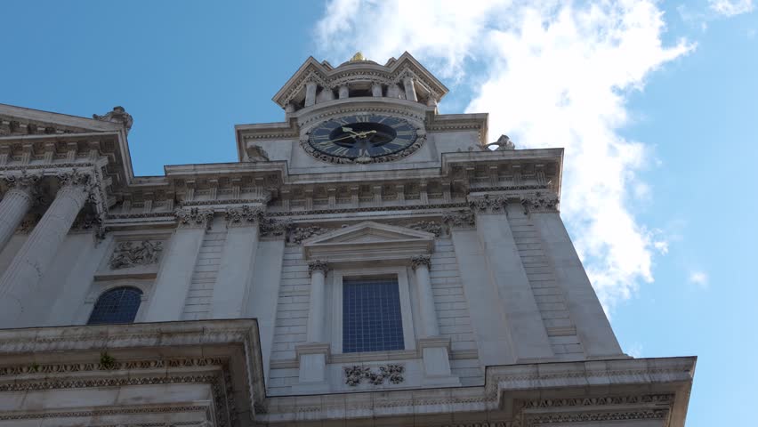 St Paul’s Cathedral in London showing the clock tower and facade from a low angle. Daytime view with architectural details and clouds in the sky