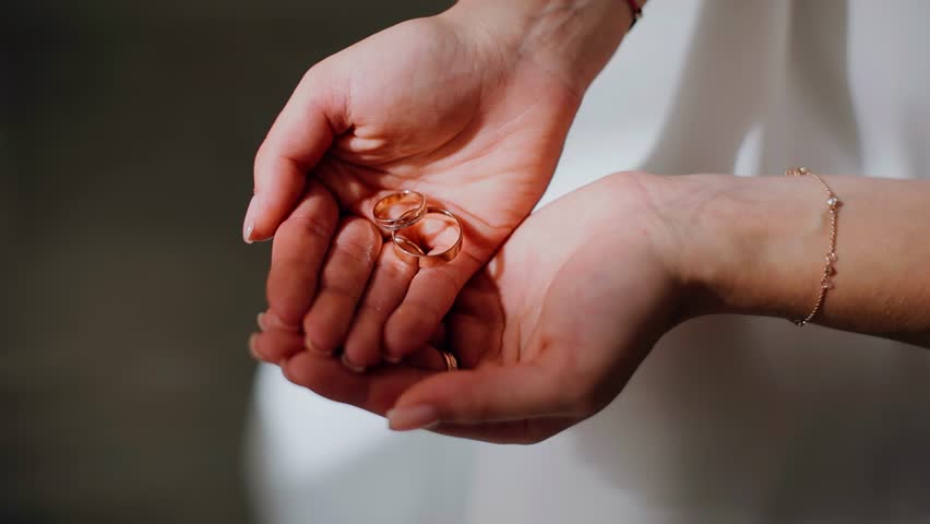 A girl clutches gold wedding rings in her palms. Close-up shooting