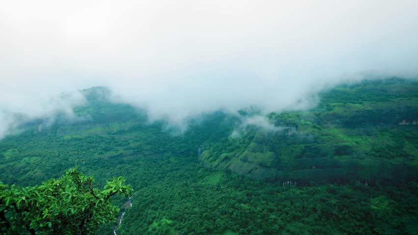 4K Aerial view of Sahyadri hills covered by lush green forest and clouds in sky during monsoon season at Maharashtra, India. Nature landscape. Mesmerizing view of green Western Ghats.  