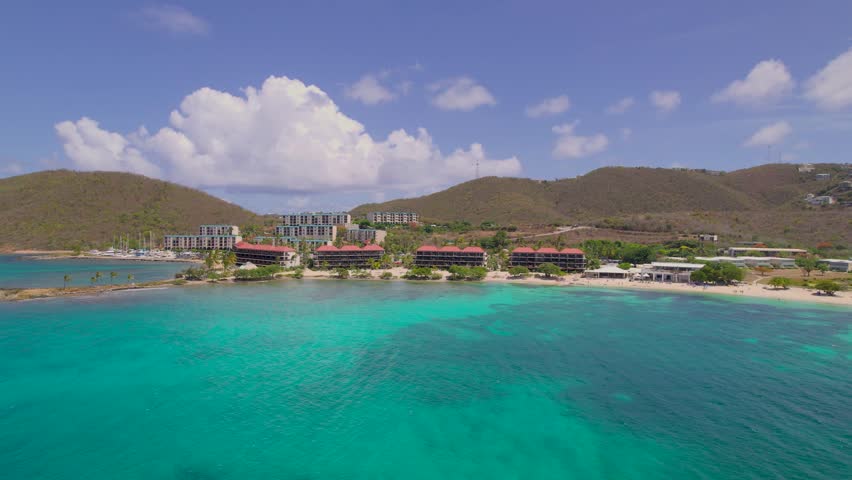 Aerial drone shot of turquoise water and beachfront resort buildings along hillside coast in St. Thomas, US Virgin Islands.