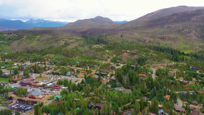 Drone shot over Flathead Lake Montana region showing cabins, rolling forest regrowth, winding roads, and expansive mountain terrain across a scenic alpine valley