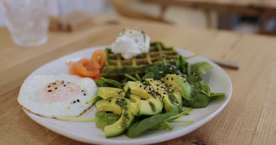 Person eating healthy breakfast with avocado, egg and spinach waffles