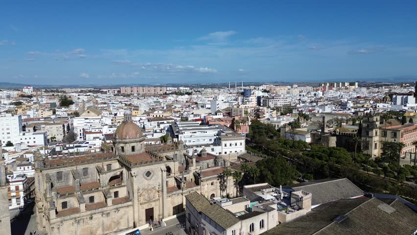Aerial drone shot moving laterally in 4K resolution showing a close up panoramic view of the Jerez Cathedral bell tower and the old town district under a clear sunny sky