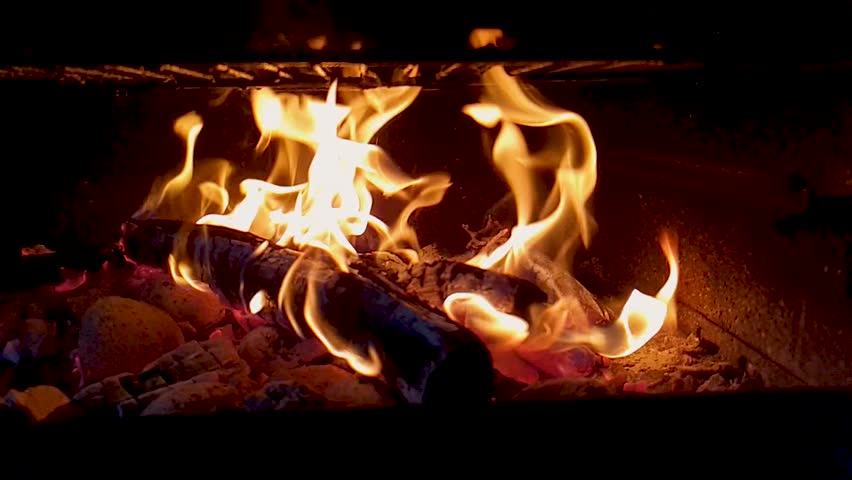 Close up of a wood log burning with bright golden flames and red hot glowing coals in a dark fireplace