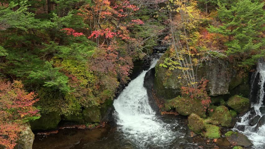Beautiful waterfall flowing through rocks surrounded by vibrant autumn foliage in Nikko Japan scenic nature landscape