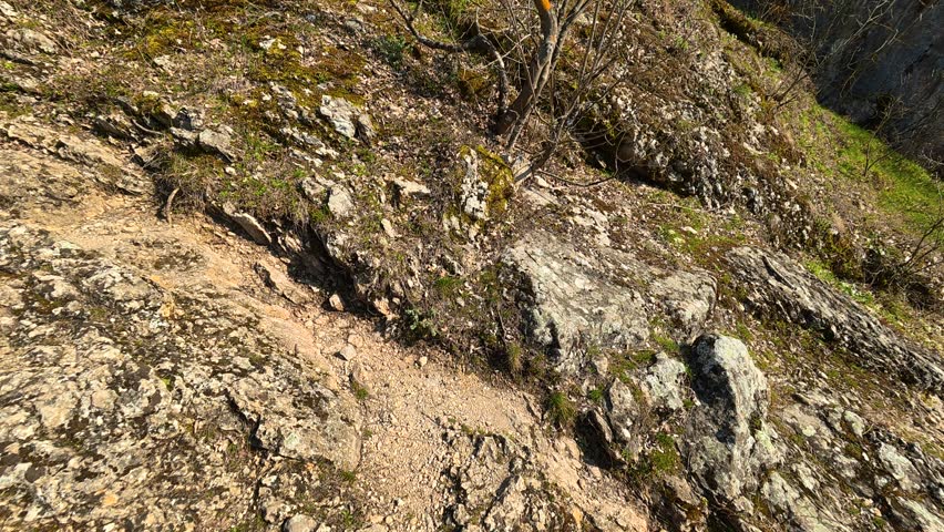 Low angle shot of a rocky hill with a medieval tower or watchtower on top. Filmed from below looking upward, creating a dramatic perspective. Autumn setting with clear sky and sunlight highlighting the natural landscape and historic structure. Ideal for documentary, history, and travel footage.