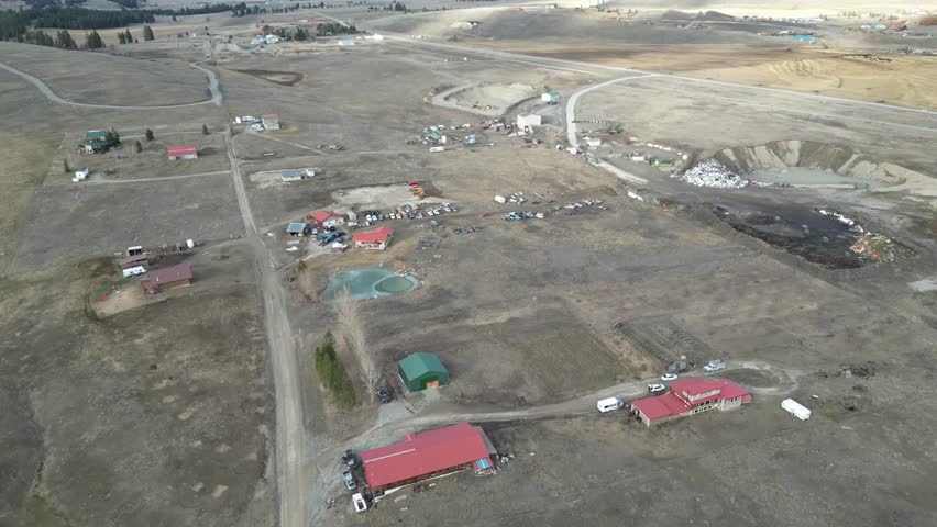 Drone footage of a rural Montana landscape featuring farm buildings equipment and industrial zones under a bright sky for logistics and real estate