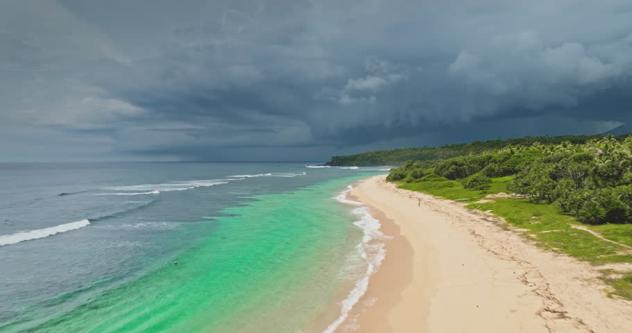 Drone flight over pristine white sand beach and turquoise water and lush tropical vegetation at Port Resolution on Tanna Island, Vanuatu, where dark storm clouds gather overhead. Wild nature landscape