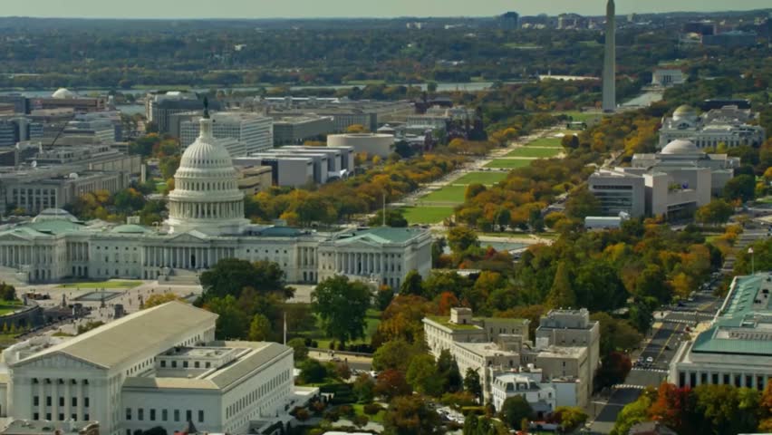 Drone footage of the National Mall in Washington, D.C., showcasing the United States Capitol in the foreground with its iconic dome and neoclassical architecture. The aerial view extends toward the Washington Monument in the background, framed by tree-lined avenues, museums, and government buildings. This cinematic perspective highlights the historic, cultural, and political significance of America’s capital city.