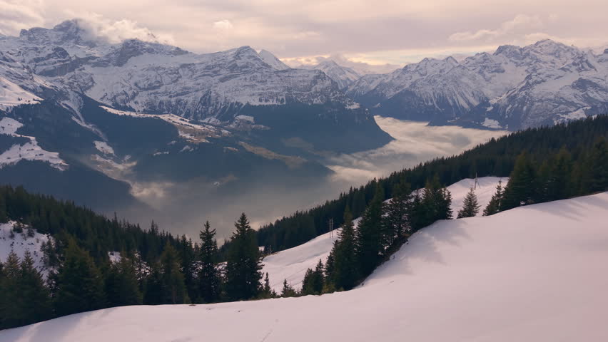 Peaceful sunrise over mountain range with fog. Aerial shot of snowy peaks at dawn with clouds