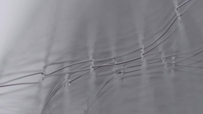 Macro shot of water droplets forming and clinging to a wire mesh fence, with a shallow depth of field creating an abstract, grey, and moody background texture.