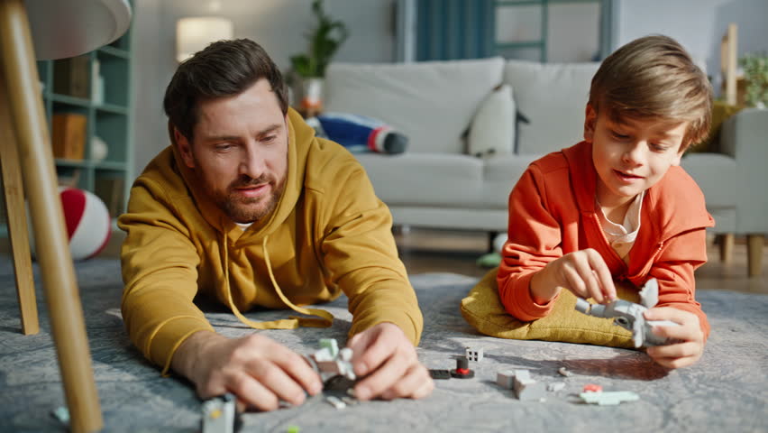 Father son building blocks  lying living room floor closeup. Smiling bearded man playing toy plane talking little boy enjoying family playtime together. Cheerful child happy daddy involved in home game.