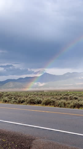 Misty sky with a rainbow near by and a quiet road with one car passing by
