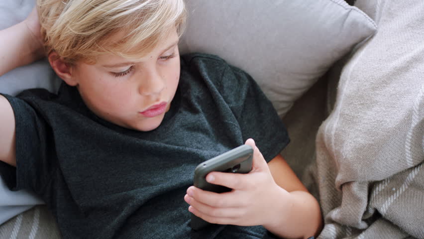 Above, gaming and phone with boy on sofa in living room of home for morning or weekend streaming. App, game and mobile with child in apartment for digital subscription or online entertainment