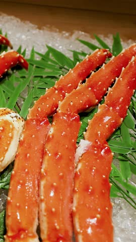 Close-up handheld shot of cooked king crab legs displayed on crushed ice with bamboo leaves