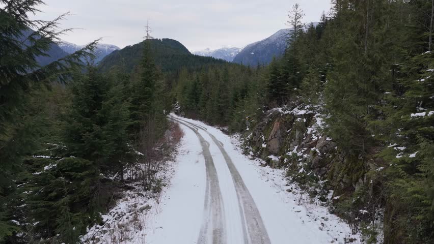 Aerial View of a Snow-Covered Forest Road Winding Through Majestic Mountains in British Columbia, Canada