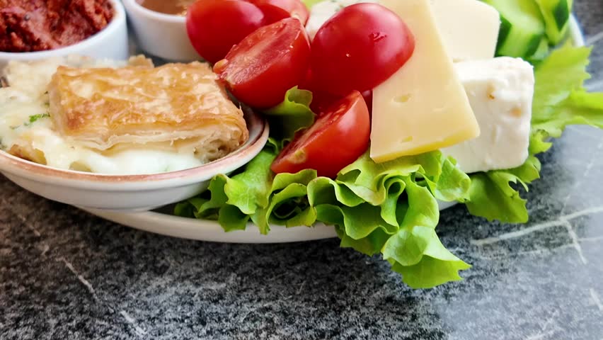 A close up view of a delicious turkish breakfast spread with various dishes including cheeses, olives, tomatoes, and pastries