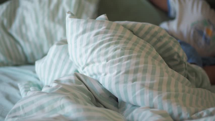 Close up of an unmade bed with crumpled sheets and pillows, showcasing a cozy and relaxed morning atmosphere with soft focus movement