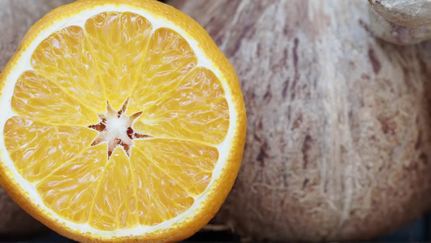Close up shot of fresh juicy orange fruit half with vibrant yellow segments slowly rotating on brown fibrous background