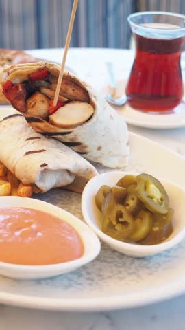 Delicious chicken wrap with fries sauce and jalapenos served on a plate with tea