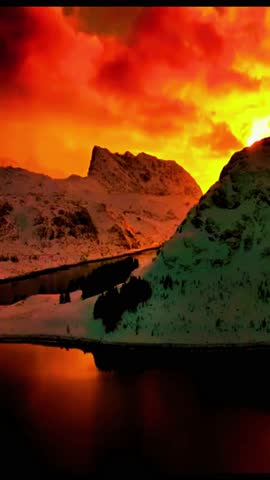  Fiery orange sunset sky over snowy mountain range reflected in a calm lake water during a beautiful winter evening, vertical view.

