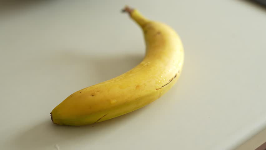A ripe yellow banana resting on a clean white surface