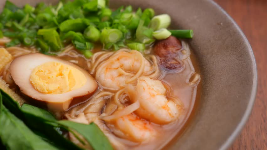 Close up shot of delicious shrimp ramen bowl with noodles egg and fresh greens moving gently