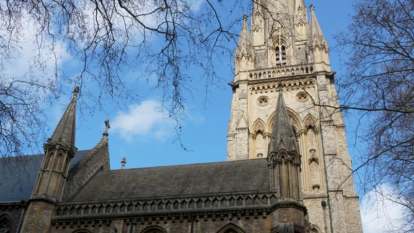 St Mary Abbots Church in Kensington London with tall stone tower and gothic facade. Daytime view showing architectural details against blue sky