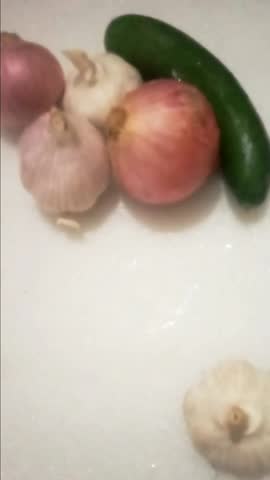 Fresh vegetables including red onions, garlic bulbs, and a green cucumber on a white background.